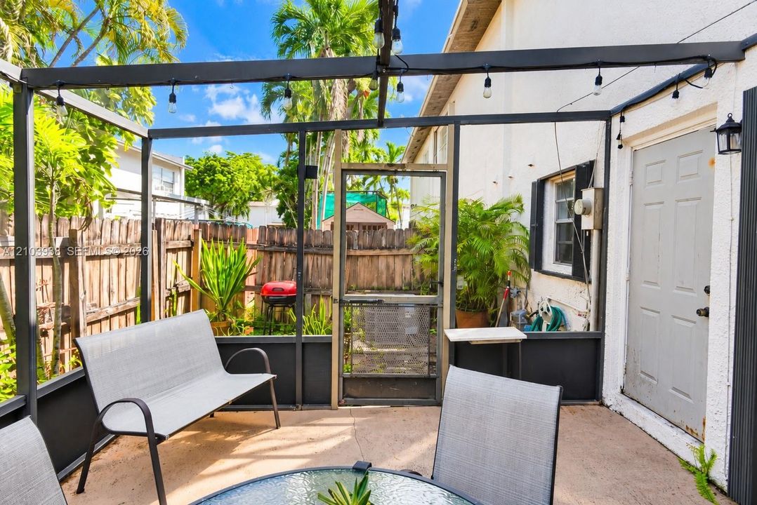 Screened-in patio featuring a concrete floor, dark metal structural framing, exterior wall-mounted lighting, and a wood privacy fence