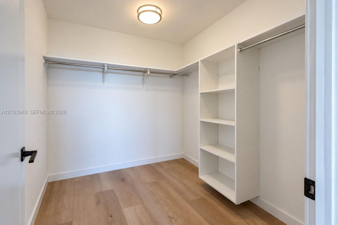 Walk-in closet featuring white built-in shelving, integrated metal hanging rods, wood-finish flooring, and a flush-mount ceiling light
