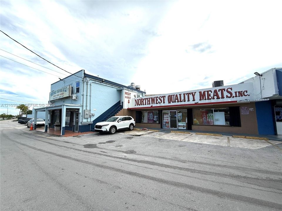Commercial property exterior featuring a multi-unit building with storefront glass displays, a designated asphalt parking area, and an external staircase