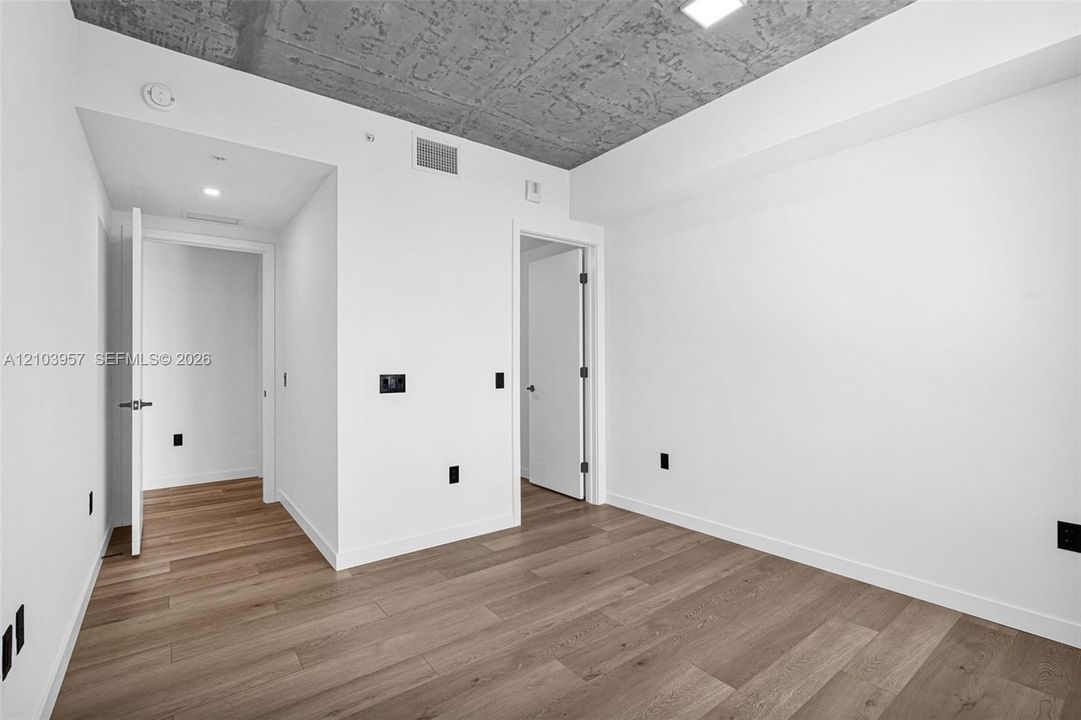 Hardwood-style flooring throughout, smooth white walls, recessed lighting, and a textured concrete ceiling