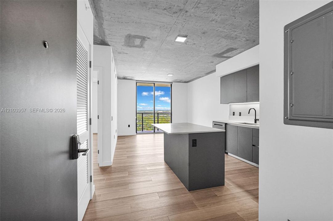 Open concept living space featuring wood-finish flooring, a contemporary kitchen with dark cabinetry and a center island, and a concrete ceiling