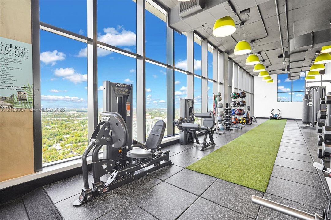 Floor-to-ceiling windows, high ceilings with exposed ductwork, modern pendant lighting, resilient rubber flooring, and an artificial turf track