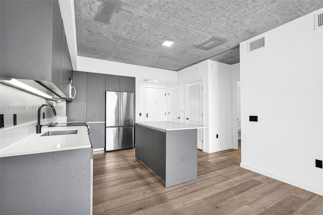 Modern kitchen featuring a stainless steel refrigerator, matte black faucet, light wood-finish flooring, and a concrete-finish ceiling