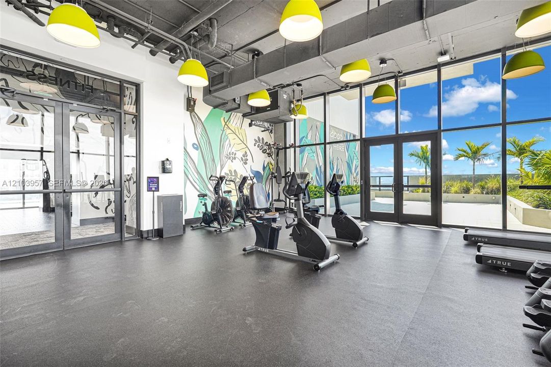 Expansive fitness room featuring a full wall of floor-to-ceiling windows, direct outdoor access, contemporary pendant lighting, and a decorative accent wall
