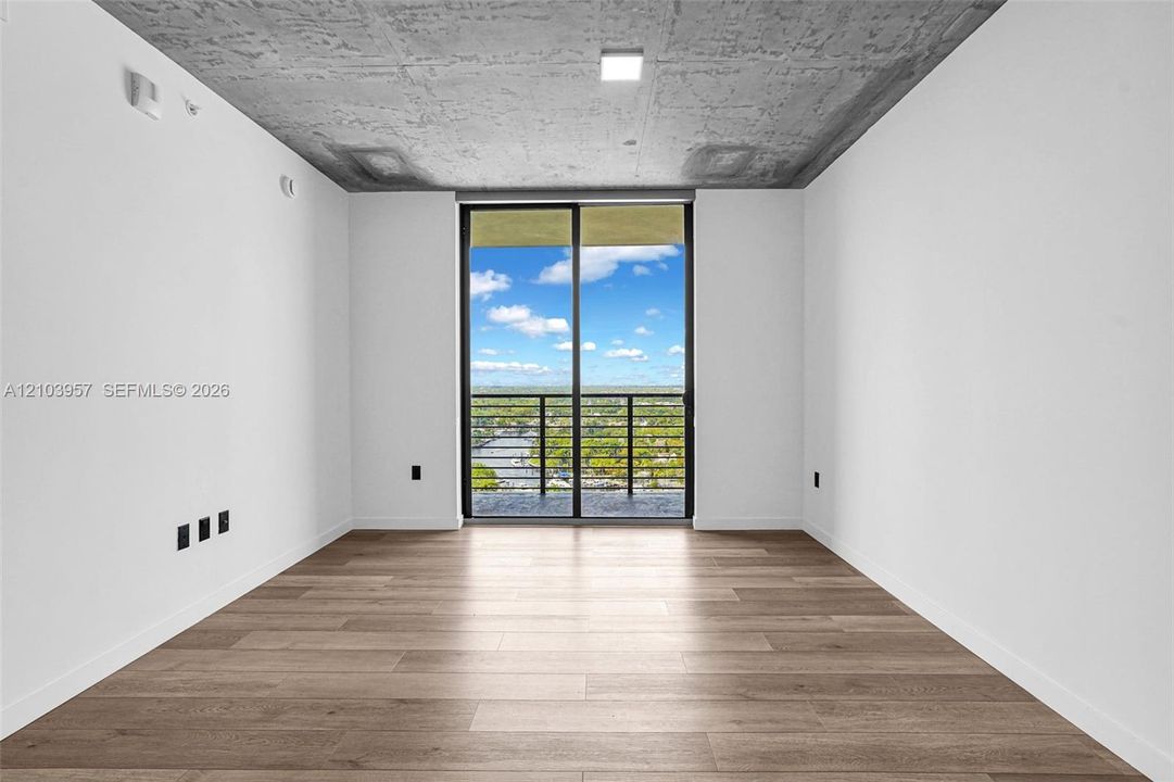 Expansive room with wood-finish flooring, a full-height glass sliding door, and a private balcony with metal railings