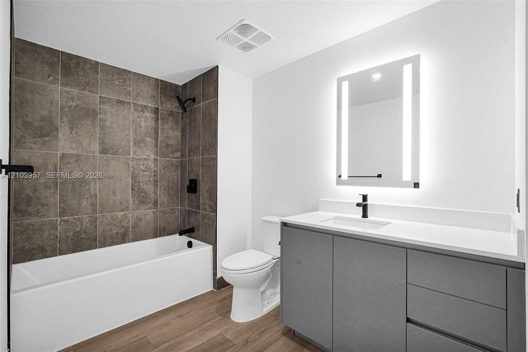 White bathtub with dark-toned tile surround, matte black fixtures, and a wood-finish floor