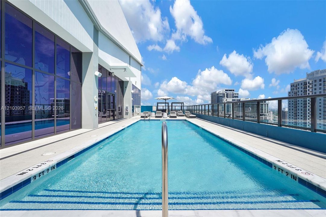 Rooftop swimming pool with integrated steps, glass panel railing, and surrounding paver decking
