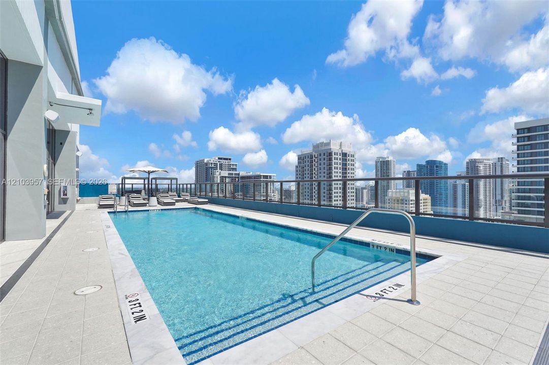 Rooftop swimming pool featuring a city backdrop, clear blue water, and a glass-paneled railing