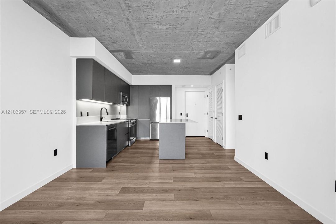 Modern kitchen featuring dark cabinetry, stainless steel appliances, light-toned countertops, a kitchen island, and wood-finish flooring