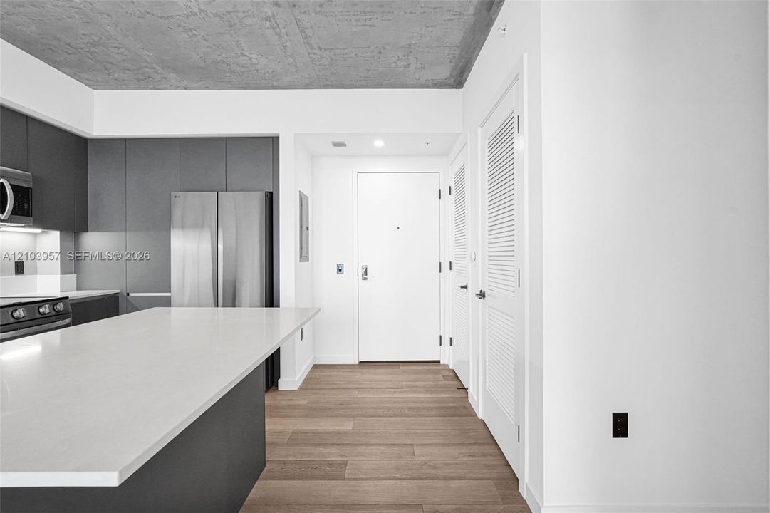 Kitchen featuring a large island with a white countertop, dark flat-panel cabinetry, stainless steel appliances, and a wood-finish floor