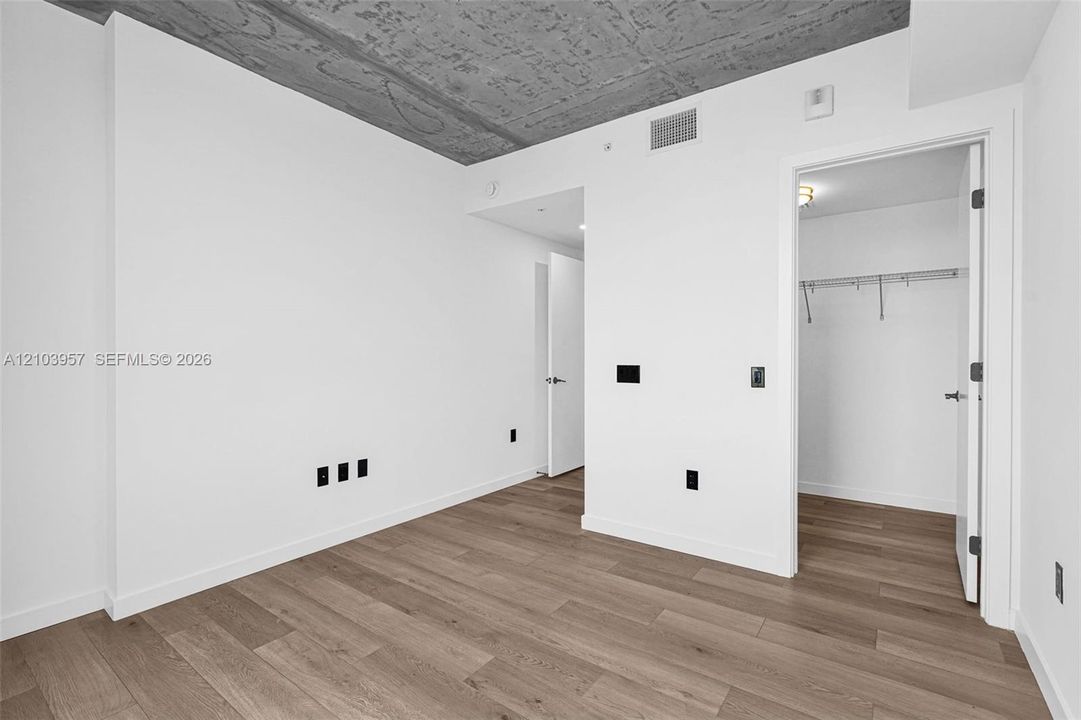 Wood-finish flooring, white walls, exposed concrete ceiling, recessed lighting, and a closet with built-in shelving