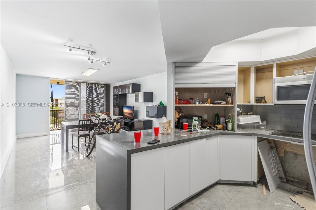 Kitchen featuring a peninsula with a metallic-finish countertop, white cabinetry, a built-in microwave, and glossy tile flooring