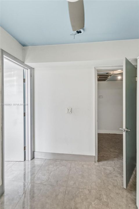 Neutral-toned tile flooring, light blue ceiling, and solid-core interior doors with metallic hardware