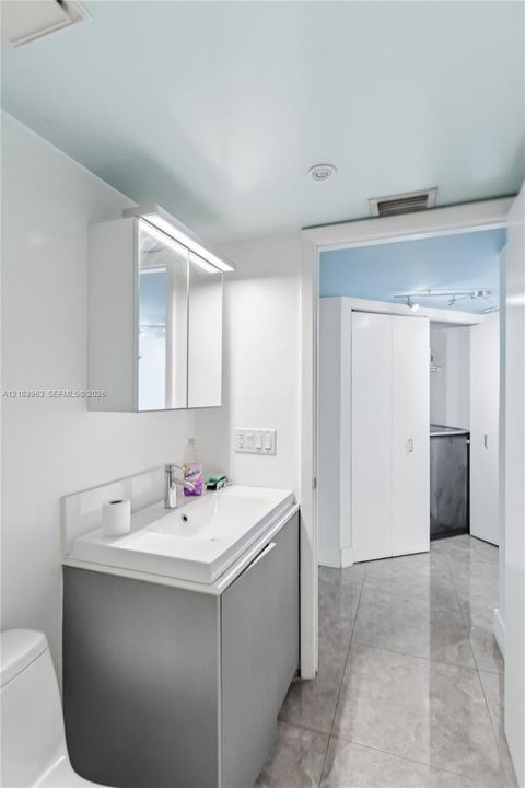 Modern vanity featuring a rectangular integrated sink, neutral cabinetry, and an illuminated mirrored medicine cabinet, complemented by large-format tile flooring