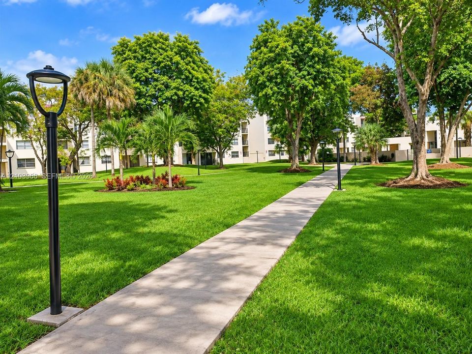 Expansive landscaped grounds featuring manicured lawns, mature specimen trees, established palm plantings, and concrete walkways illuminated by fixed post lighting