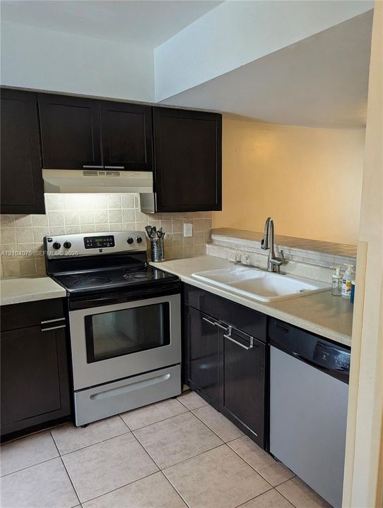 Kitchen featuring dark cabinetry, stainless steel appliances, ceramic tile backsplash, and light-toned countertops