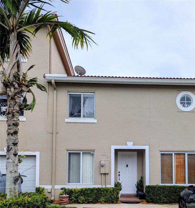 Stucco exterior facade featuring a tile roof, decorative circular accent window, multi-panel front door, and manicured shrubbery