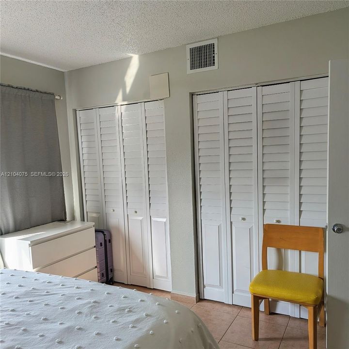 Dual closets featuring white louvered bi-fold doors and tile flooring