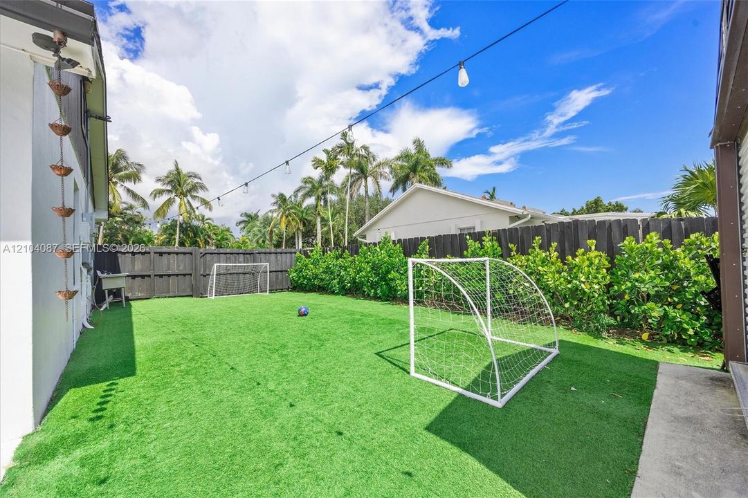 Fenced backyard with artificial turf, mature palms, and string lighting