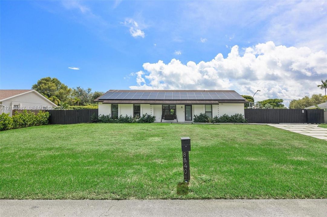 White exterior with dark trim accents, solar panel array, black fence, and a paver driveway