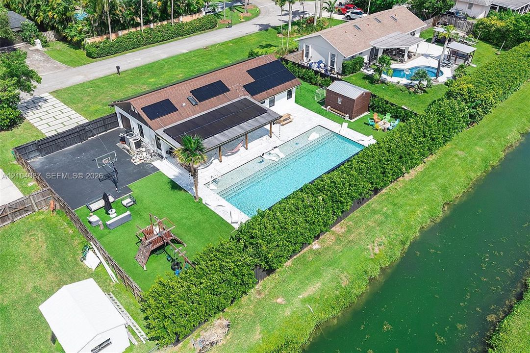 Exterior featuring a large in-ground swimming pool, covered patio, sport court, and artificial turf lawn