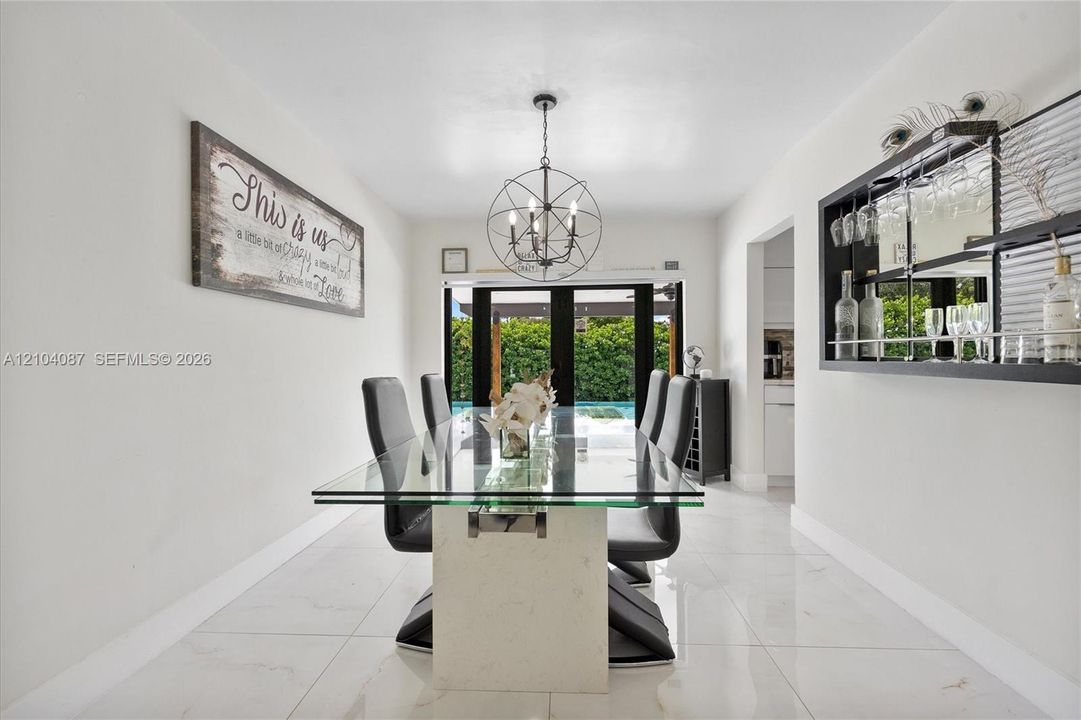 Recessed lighting, large format tile flooring, black multi-pane exterior doors, and a built-in wall bar with mirrored backing