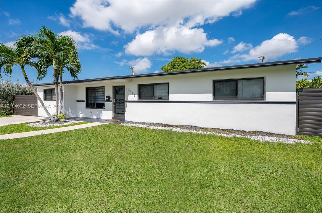 Single-story exterior featuring white stucco finish, dark-toned trim, sliding glass windows, and metal side fencing