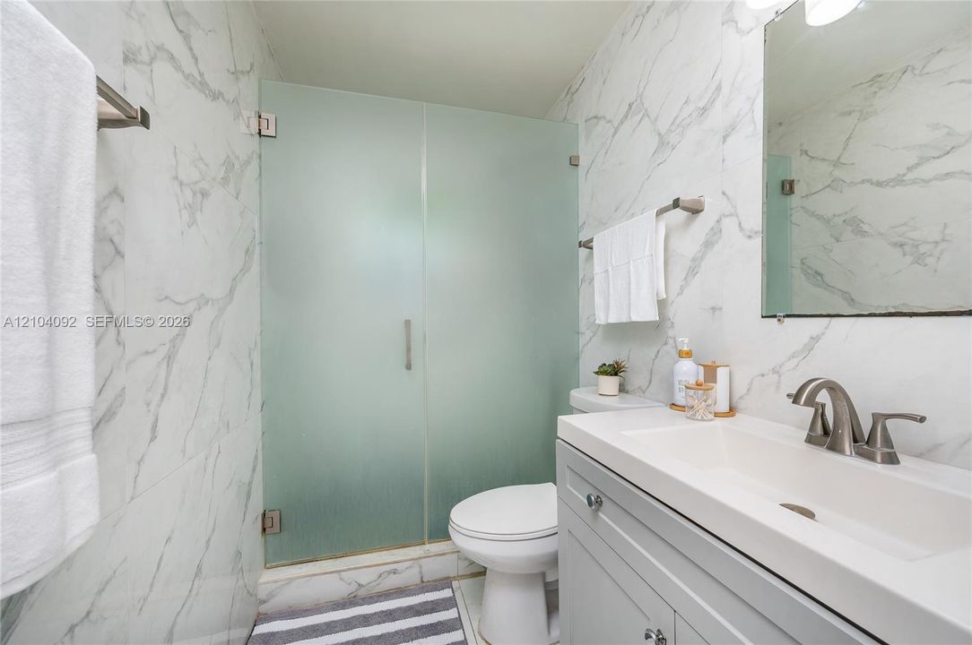 Bathroom featuring full-height stone-patterned wall tiling, a light gray vanity cabinet, a rectangular integrated sink with a brushed-nickel faucet, and a frosted glass shower enclosure