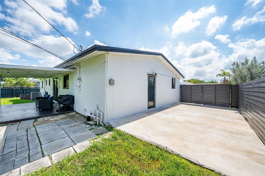 White stucco exterior featuring a covered patio, paved side area, and a horizontal metal privacy fence