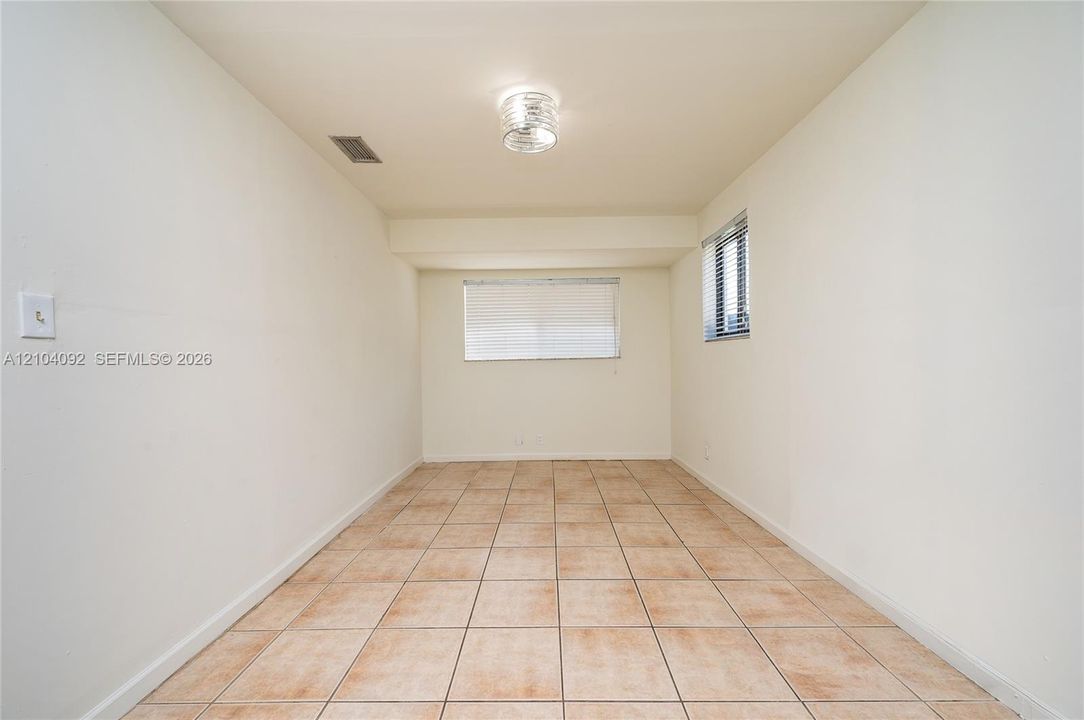 Neutral-toned interior space featuring light-colored ceramic tile flooring, neutral wall paint, a flush-mount circular ceiling fixture, and dual windows with horizontal blinds