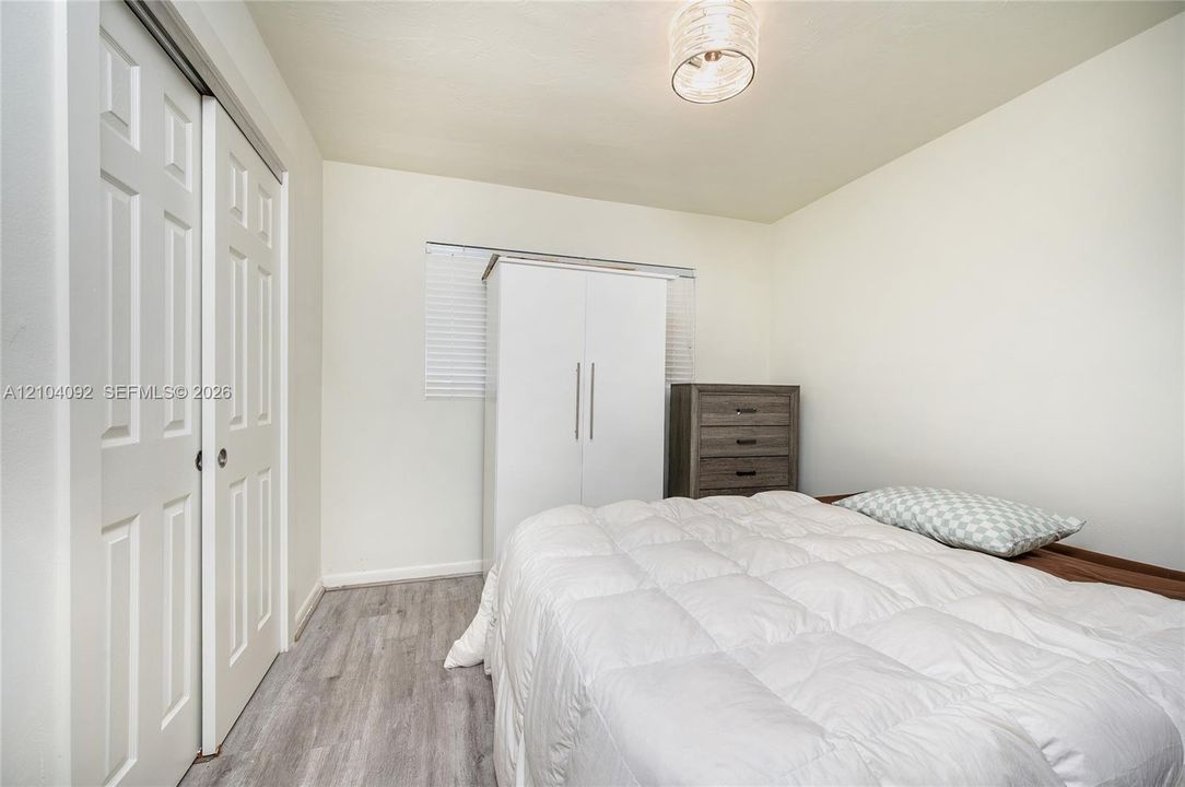 Wood-finish flooring, double-panel sliding closet doors, ceiling-mounted drum light fixture, and window blinds