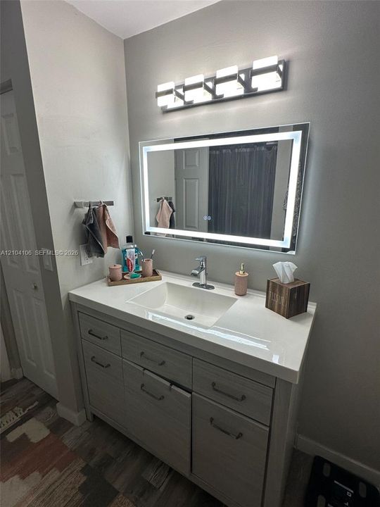 Modern vanity featuring a rectangular integrated sink, quartz countertop, wood-finish cabinetry, a rectangular LED-backlit mirror, and a four-light fixture