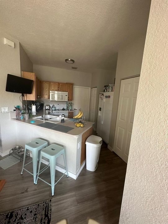 Kitchen featuring wood cabinetry, laminate countertops, a double-basin sink with a gooseneck faucet, an over-the-range microwave, and wood-finish flooring