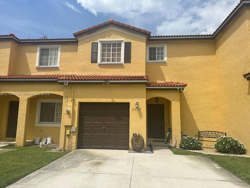 Stucco exterior featuring a terra cotta tile roof, recessed entryway, attached garage, and divided-lite windows with dark shutters