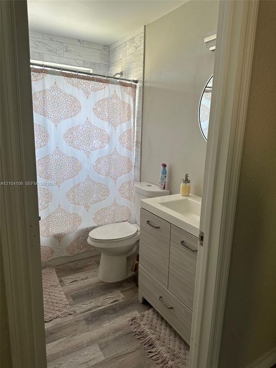 Bathroom featuring a wood-finish vanity with an integrated sink, wood-finish flooring, and a tub enclosure with tile-patterned wall surround