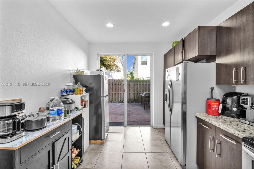 Kitchen with tile flooring, recessed lighting, wood-finish cabinetry, and a sliding glass door to a paved patio