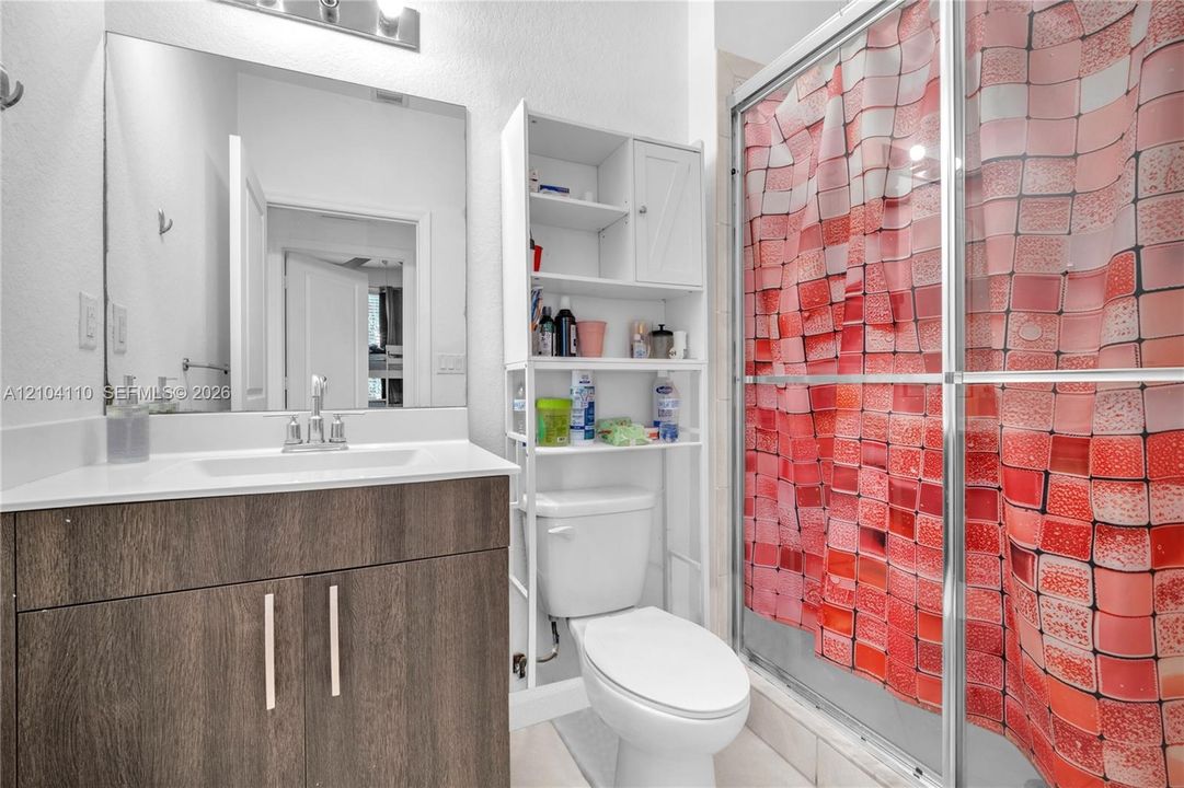 Bathroom featuring a wood-finish vanity with an integrated sink, a large wall mirror, and a shower with a sliding glass enclosure