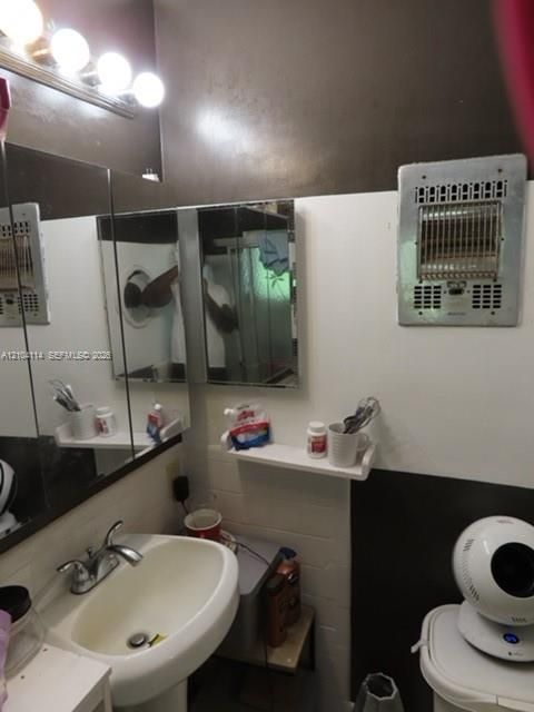 Wall-mounted vanity mirror, pedestal sink with dual-handle faucet, integrated wall-mounted heater, and multi-bulb vanity light fixture