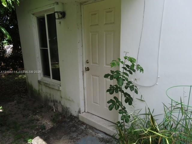 Exterior entrance featuring a light-toned door with a multi-panel design, a sliding window with a screen, and a wall-mounted light fixture