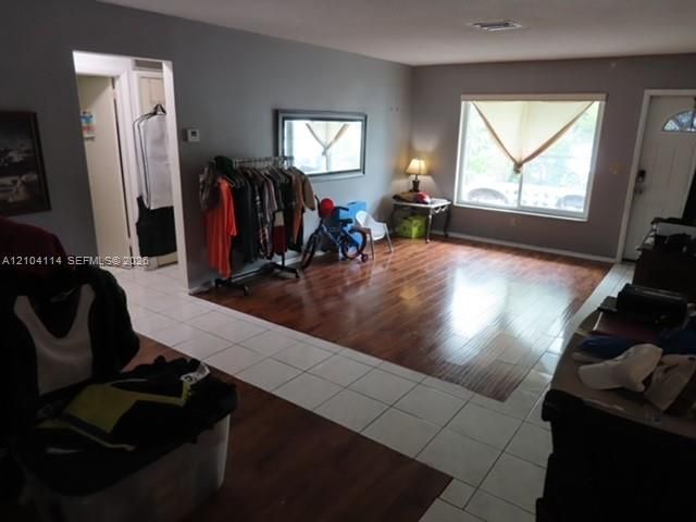 Living area featuring wood-finish flooring, white tile entryway, large window, and solid core entry door