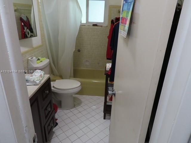 Bathroom featuring a dark wood-finish vanity, light-toned countertop, white tile flooring, and integrated tub and shower surround