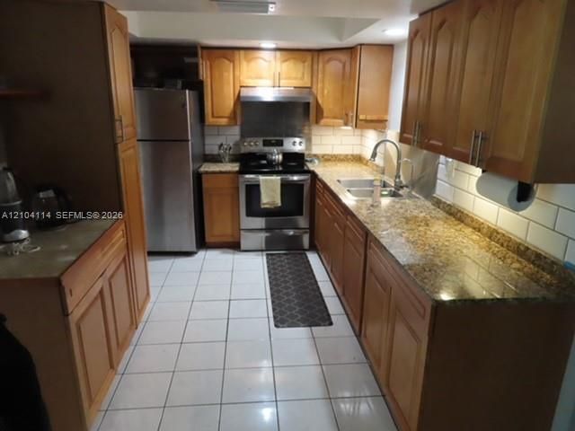 Kitchen featuring shaker-style wood cabinetry, stone countertops, stainless steel appliances, ceramic tile backsplash, and ceramic floor tiling