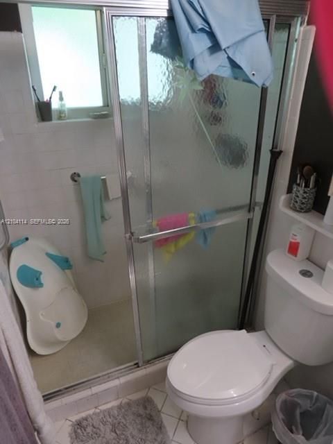 Shower enclosure with textured glass sliding doors and white tile surround, accompanied by a white porcelain toilet and integrated wall shelving