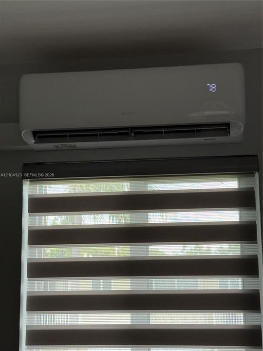 Wall-mounted ductless climate control unit with digital display and horizontally striped dual-layer window treatments