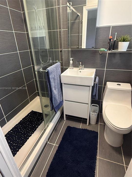 Full-tile charcoal wall and floor surfacing, glass-enclosed shower, pedestal-style vanity with rectangular basin, and single-piece toilet