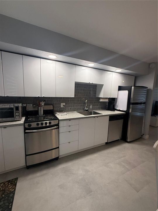 Kitchen featuring white slab-front cabinetry, stone-finish countertops, stainless steel appliances, brick-style tile backsplash, and neutral tile flooring