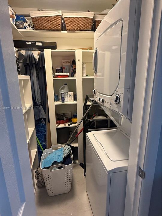 Laundry closet featuring a white stacked washer and dryer unit, built-in shelving, and overhead storage space