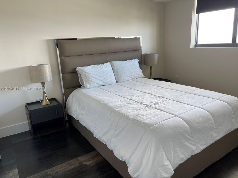 Neutral-toned walls paired with dark wood-finish flooring and a single-pane window featuring a retractable shade