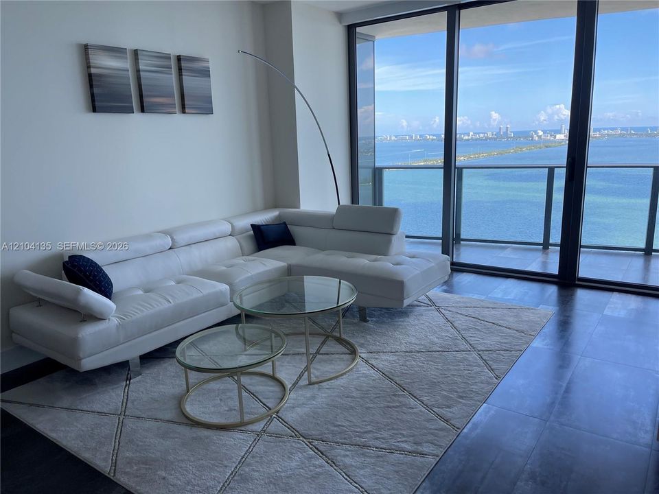 Floor-to-ceiling glass walls, dark wide-plank flooring, and expansive water and skyline scenery