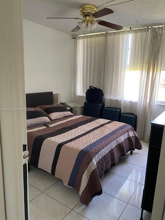 Room featuring large-format tile flooring, a multi-blade ceiling fan with integrated lighting, and wall-to-wall windows draped with floor-length curtains